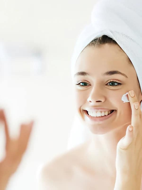 Chica sonriendo mientras aplica crema en la cara para apollo de la entrada de junio, El envejecimiento de la pie.